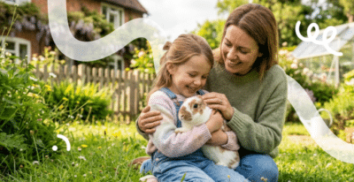 Een moeder zit met haar dochter in het gras in de tuin met hun konijn te knuffelen